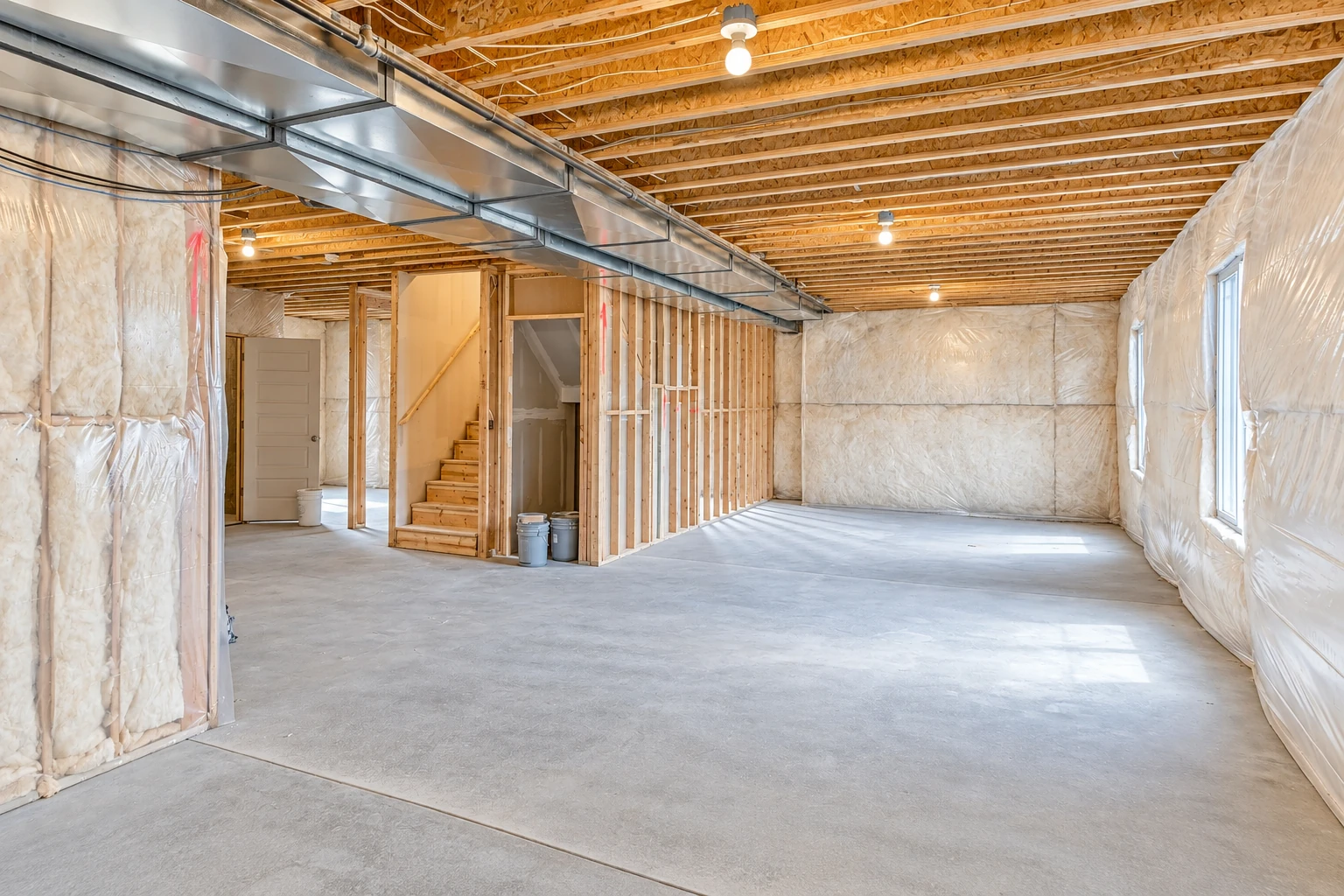 Unfinished basement with fiberglass insulation between wall studs and across the walls, beneath exposed ceiling joists and metal ductwork.