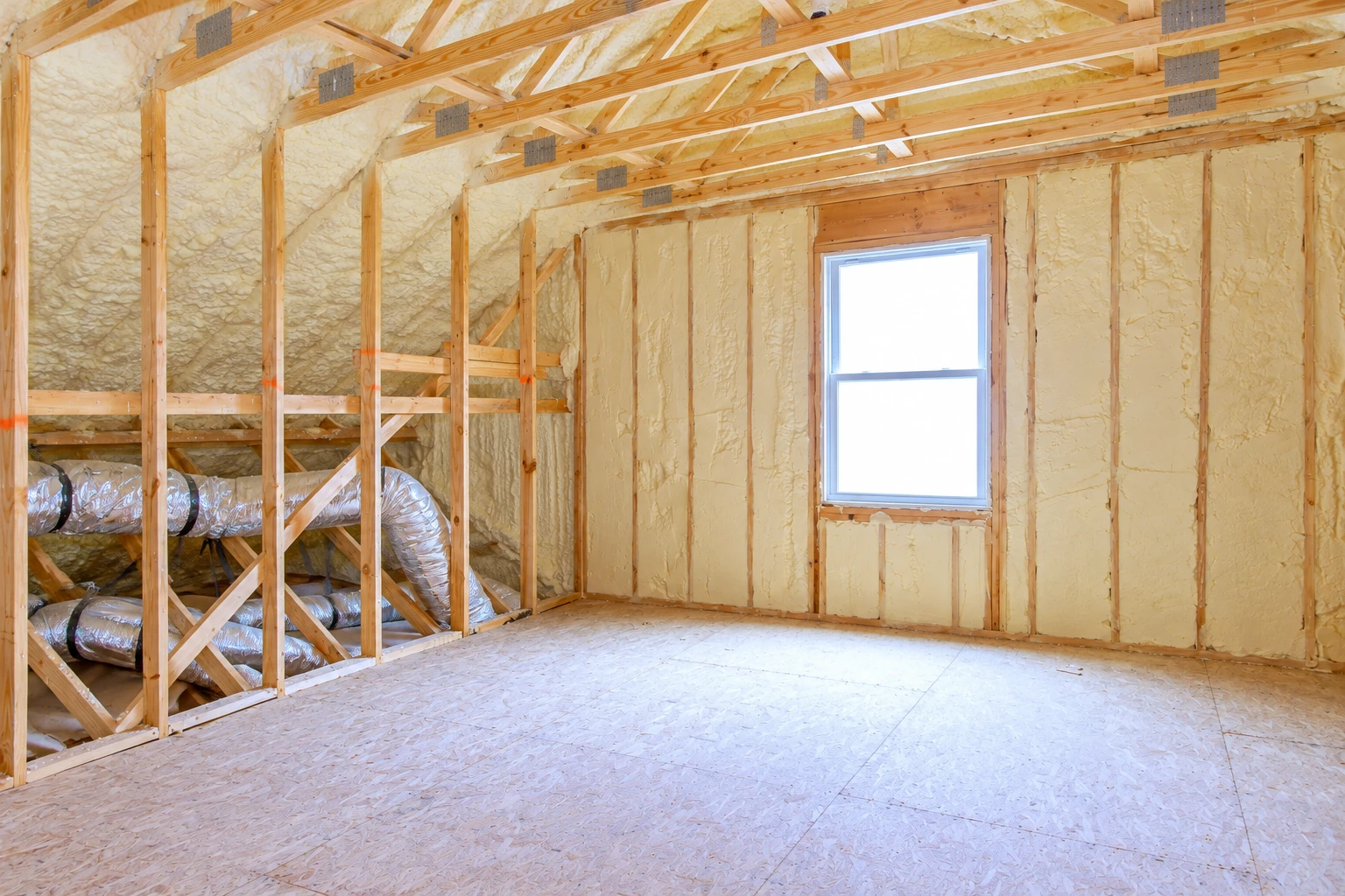 Cream-colored spray foam covers the walls and roof framing of an unfinished room with a single window.
